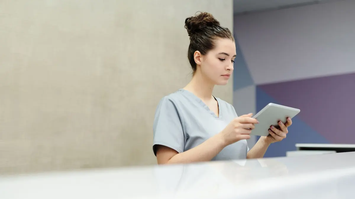 Recepcionista de clínica de uniforme olhando um tablet no balcão de atendimento