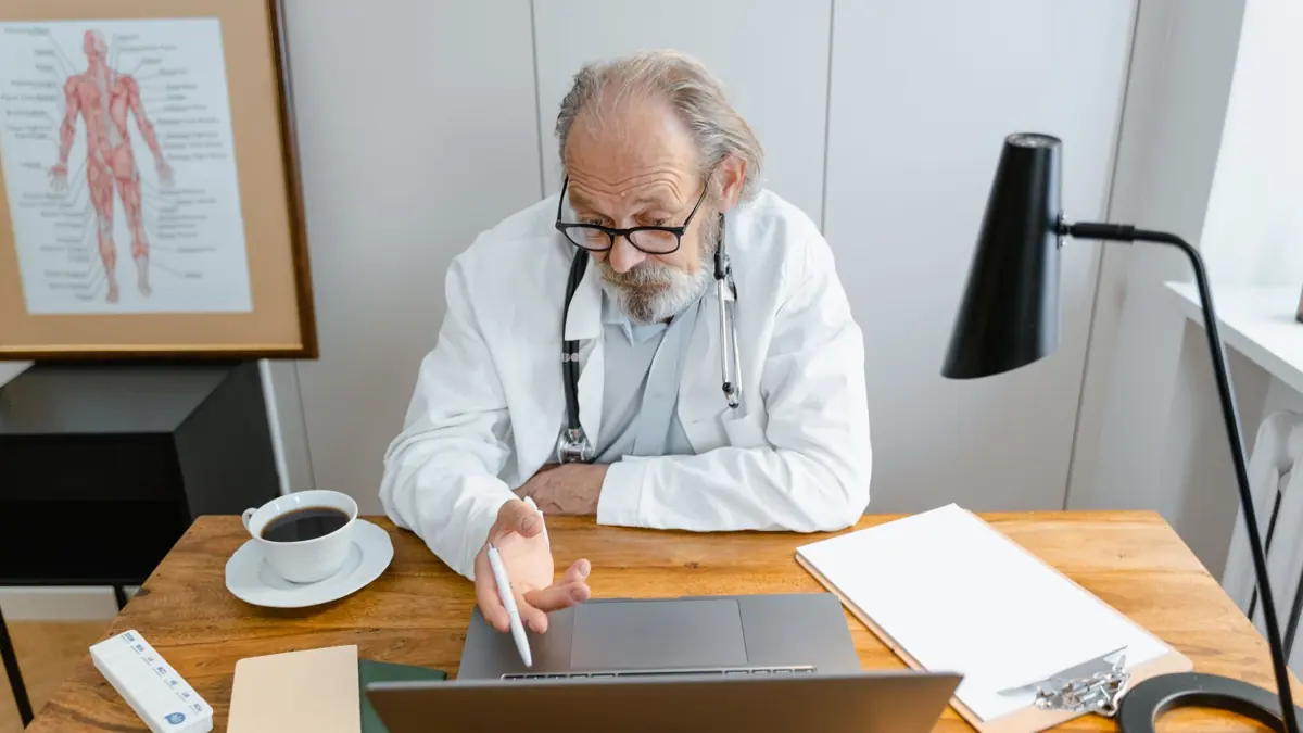 Médico de jaleco trabalhando no notebook na mesa do consultório