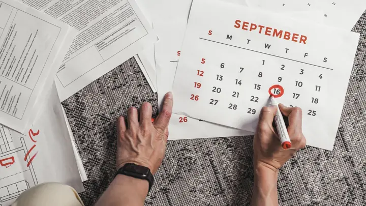 Mãos marcando uma data num calendário de papel em cima de uma mesa cheia de documentos