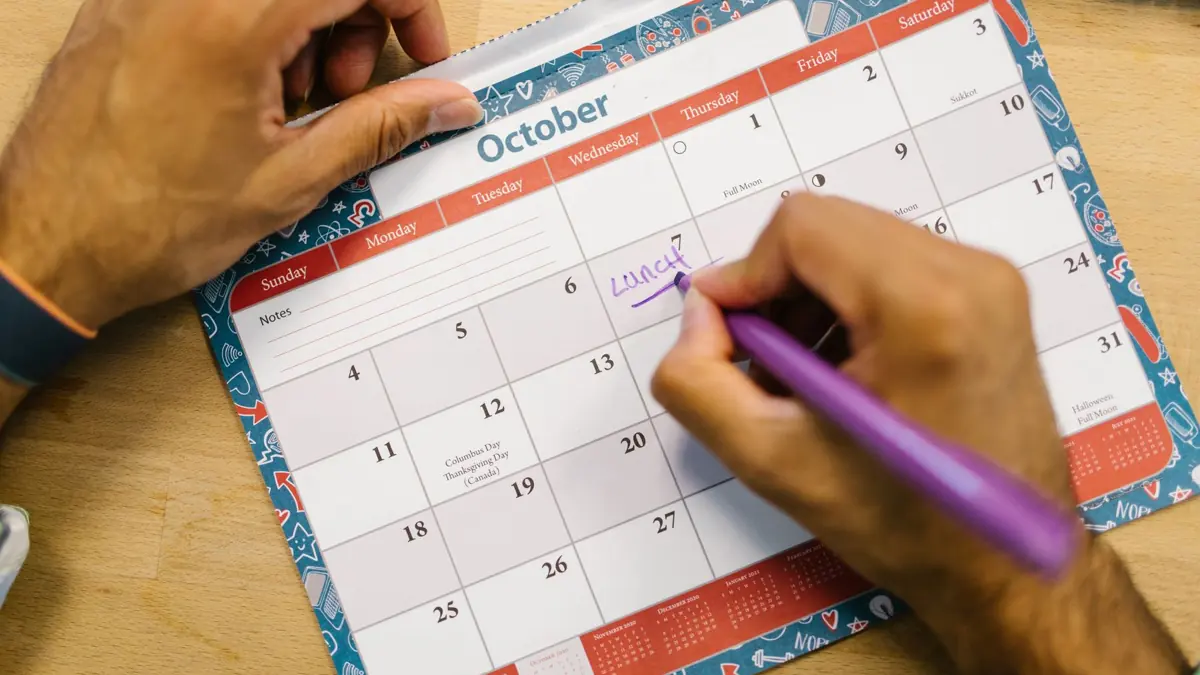 Mãos marcando uma data com caneta em um calendário de mesa