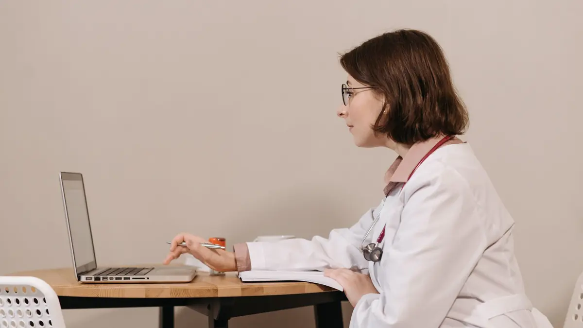Médica de jaleco usando um notebook na mesa do consultório