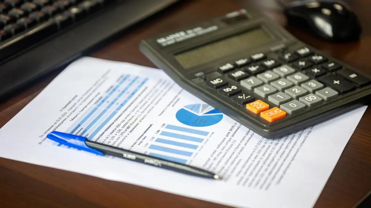 Relatório financeiro com gráficos ao lado de uma calculadora e uma caneta