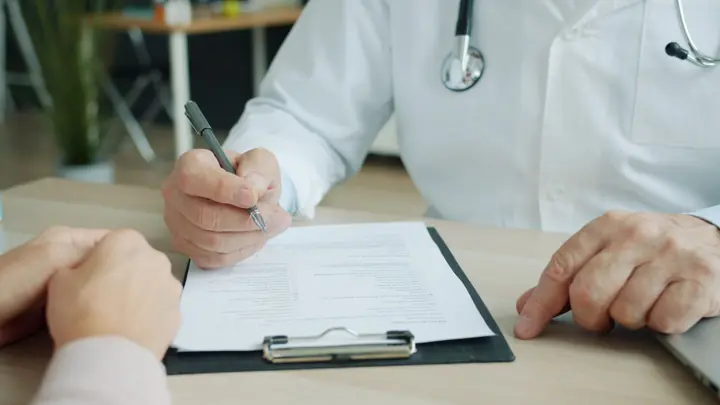 Médico de jaleco preenchendo e assinando um documento numa prancheta